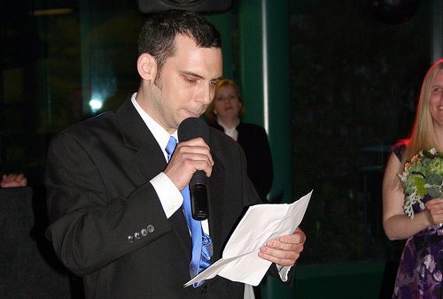 overcome fear public speaking - photo of man speaking into microphone looking at a paper speech